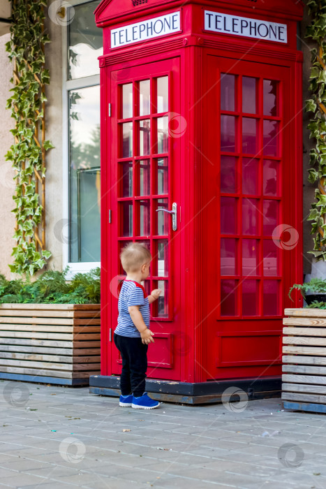 Скачать Маленький мальчик хочет войти в красную телефонную будку. фотосток Ozero