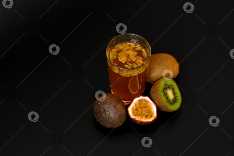 Скачать Высокий стакан свежевыжатого сока с семенами на черном фоне, рядом с кусочками спелого киви и маракуйи. фотосток Ozero