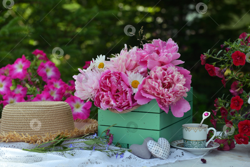 Скачать Beautiful still life with peony flowers, hat and tea cup on the table. Romantic greeting card for birthday, Valentines, Mothers Day concept. Summer background with vintage objects фотосток Ozero