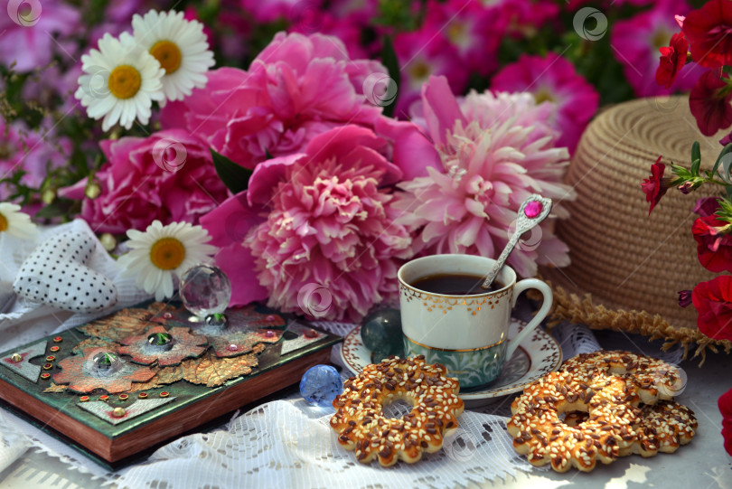 Скачать Beautiful still life with peony flowers, cup, cookies and book in the garden. Romantic greeting card for birthday, Valentines, Mothers Day concept. Summer background with vintage objects фотосток Ozero