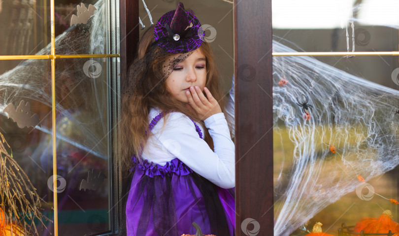 Скачать Девушка в костюме ведьмы на подоконнике у окна на вечеринке в честь Хэллоуина, украшает дом паутиной, летучими мышами, пауками, тыквами. Ужасные пейзажи, страх и ужас фотосток Ozero