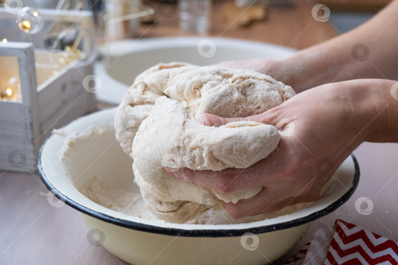 Скачать Руками замесите густое тесто на кухонном столе, украшенном праздничными украшениями к Рождеству и Новому году. Выпечка по-домашнему, аромат и уют. Крупный план фотосток Ozero