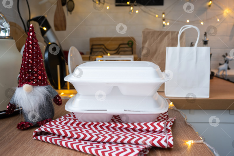 Скачать Контейнеры службы доставки еды на столе white scandi праздничная кухня в рождественском декоре. Канун Нового года, экономия времени, лень готовить, заказ горячего, одноразовая пластиковая коробка в сказочном свете. макет фотосток Ozero