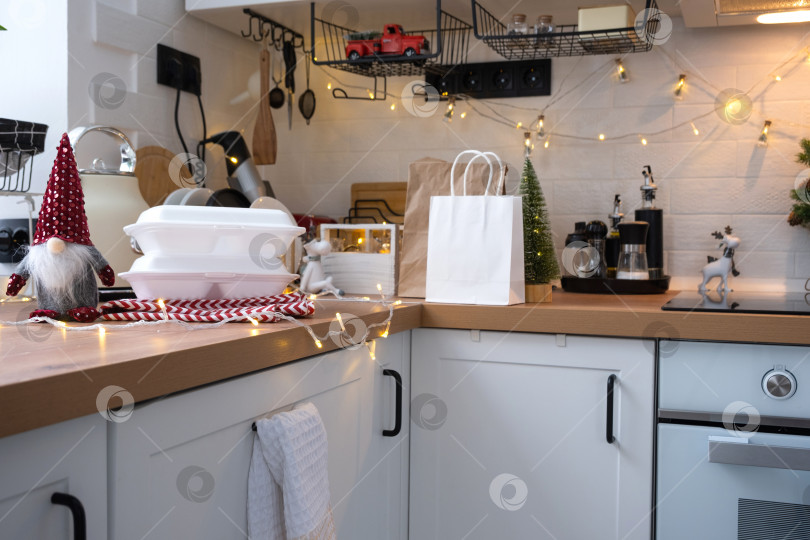 Скачать Контейнеры службы доставки еды на столе white scandi праздничная кухня в рождественском декоре. Канун Нового года, экономия времени, лень готовить, заказ горячего, одноразовая пластиковая коробка в сказочном свете. макет фотосток Ozero