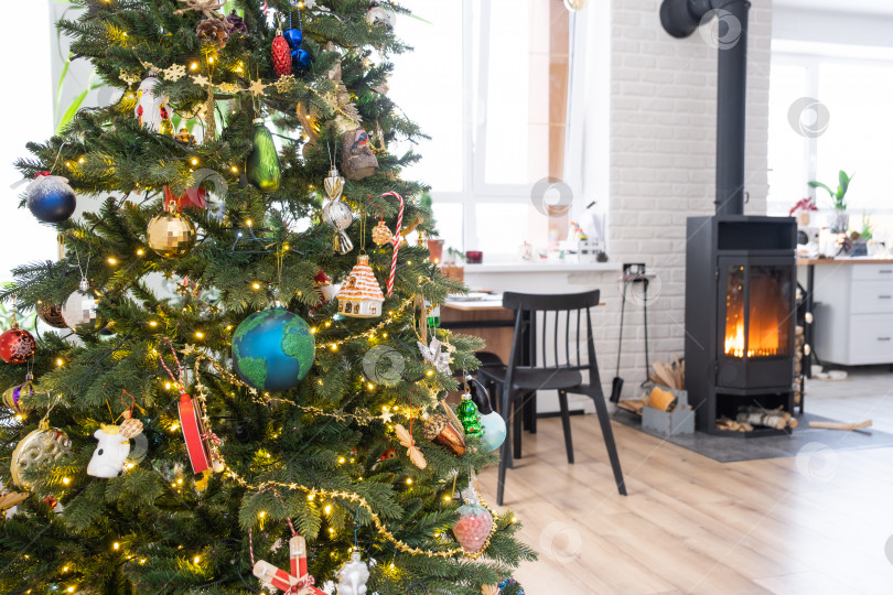 Скачать Праздничный интерьер дома оформлен к Рождеству и Новому году в стиле лофт с черной печью, камином, рождественской елкой. Теплая комната-студия с белой кухней, дровами, уютом и отоплением дома фотосток Ozero