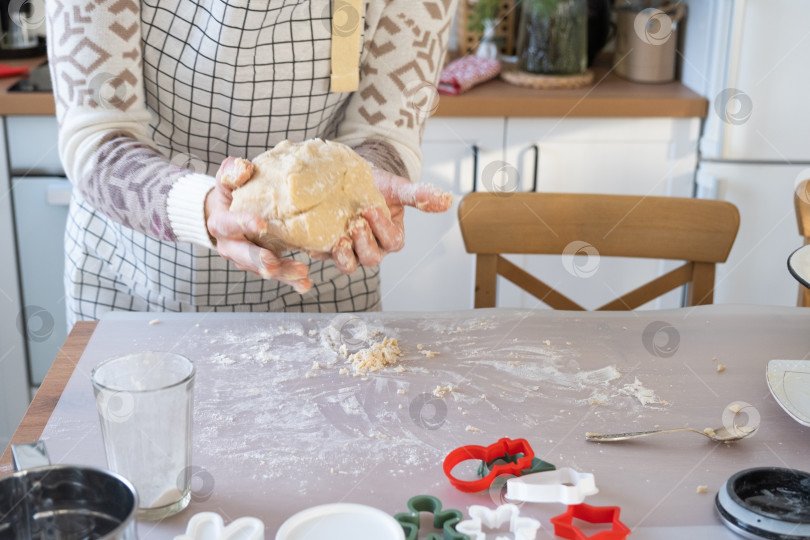Скачать Руками замесите густое тесто на кухонном столе, украшенном праздничными украшениями к Рождеству и Новому году. Выпечка по-домашнему, аромат и уют. Крупный план фотосток Ozero