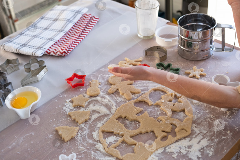 Скачать Руки мамы и дочки крупным планом вырезают печенье из теста формочками на рождественскую тематику в виде снеговика, рождественской елки, звездочек фотосток Ozero