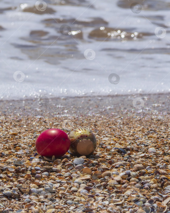 Скачать Пасхальные яйца на пляже. Пляжный фон счастливой Пасхи с крашеными яйцами на ракушках морского пляжа у кромки воды фотосток Ozero