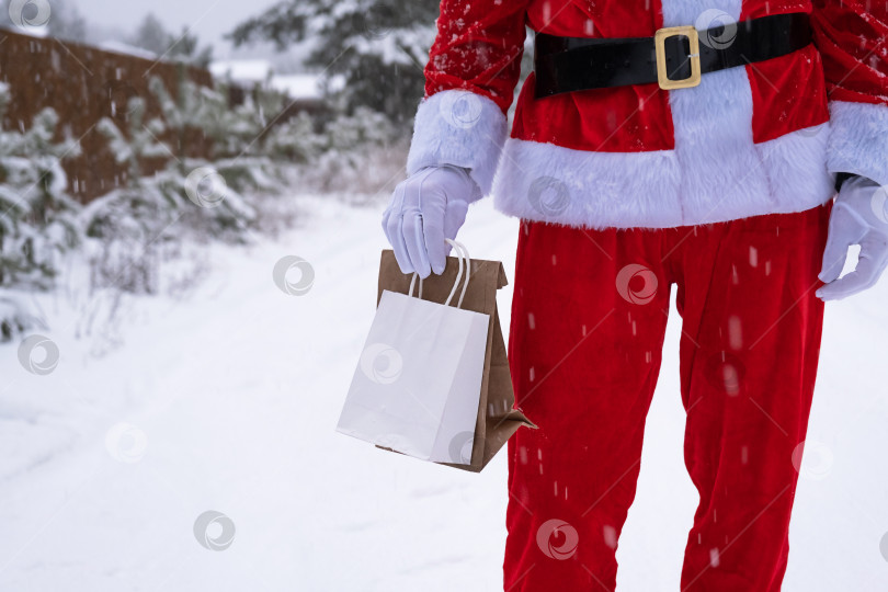 Скачать Санта-Клаус на открытом воздухе зимой и снегом вручает в ручную бумажные пакеты с подарком ручной работы, доставку еды. Покупки, переработка упаковки, ручная работа, доставка на Рождество и Новый год фотосток Ozero
