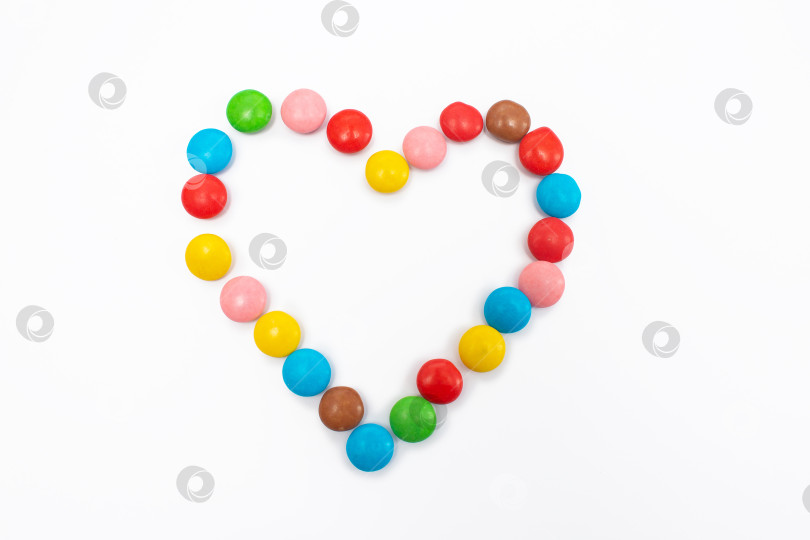 Скачать Разноцветные круглые драже-бобы, собранные в виде сердечка на белом фоне. фотосток Ozero