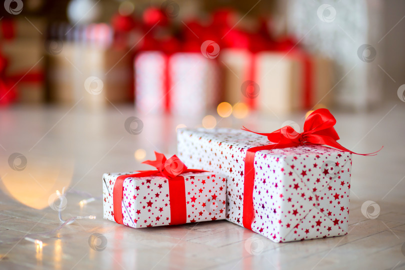 Скачать Подарок в красной упаковке лежит на полу на фоне других подарков фотосток Ozero