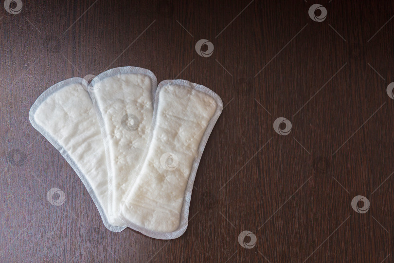 Скачать Ежедневные белые женские гигиенические прокладки лежат веером на столе на темном фоне фотосток Ozero