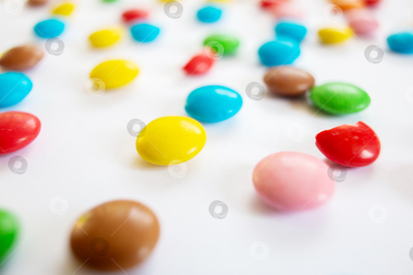 Скачать Разбросанные разноцветные маленькие круглые леденцы. Шоколадное драже в разноцветной глазури на белом фоне. фотосток Ozero