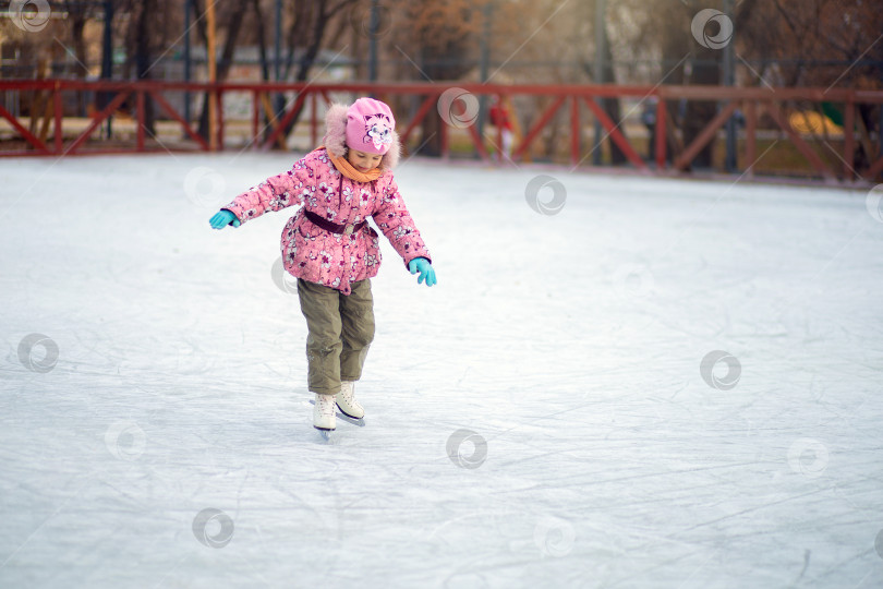 Скачать Девушка неуверенно стоит на фигурных коньках на ледовом катке и пытается кататься фотосток Ozero