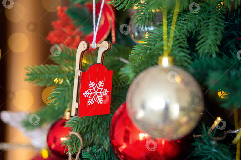 Скачать Украшение рождественской елки. Деревянная игрушка красные санки на ветке крупным планом фотосток Ozero