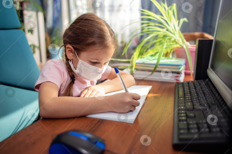 Скачать Девушка-школьница в медицинской маске делает домашнее задание перед компьютером. Карантин и дистанционное обучение фотосток Ozero