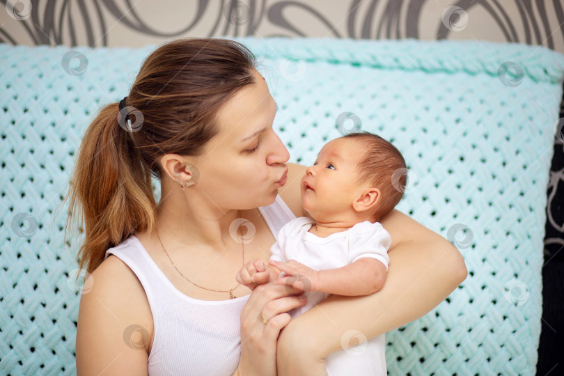 Скачать Молодая мама нежно обнимает своего новорожденного малыша. День матери. Женщина целует ребенка фотосток Ozero