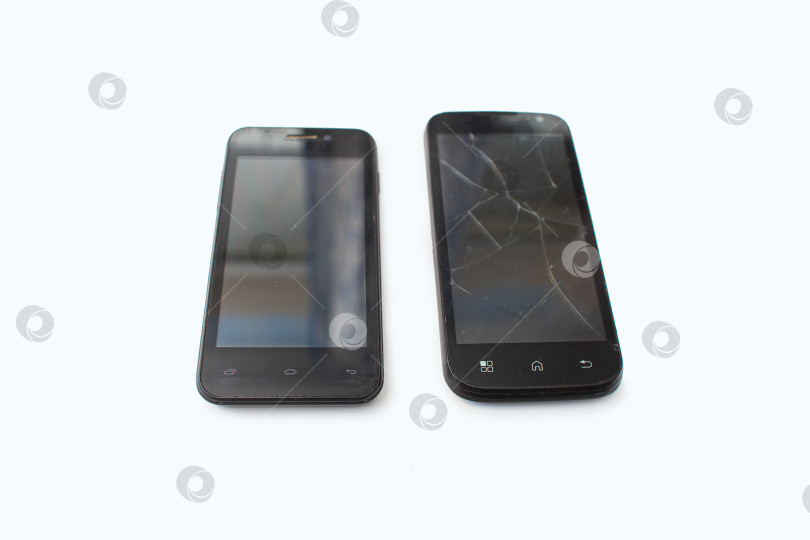 Скачать Рядом на белом фоне лежат два черных телефона. Сломанный смартфон. Трещины на экране фотосток Ozero