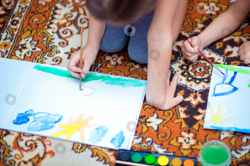 Скачать Дети дома рисуют акварелью, лежа на полу фотосток Ozero