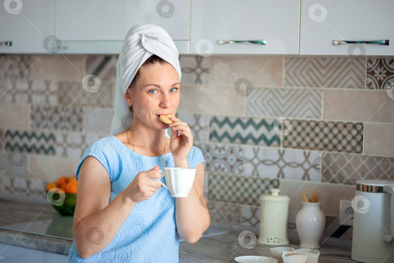 Скачать Счастливая девушка с полотенцем на голове сутра пьет кофе с печеньем на завтрак на своей собственной кухне фотосток Ozero
