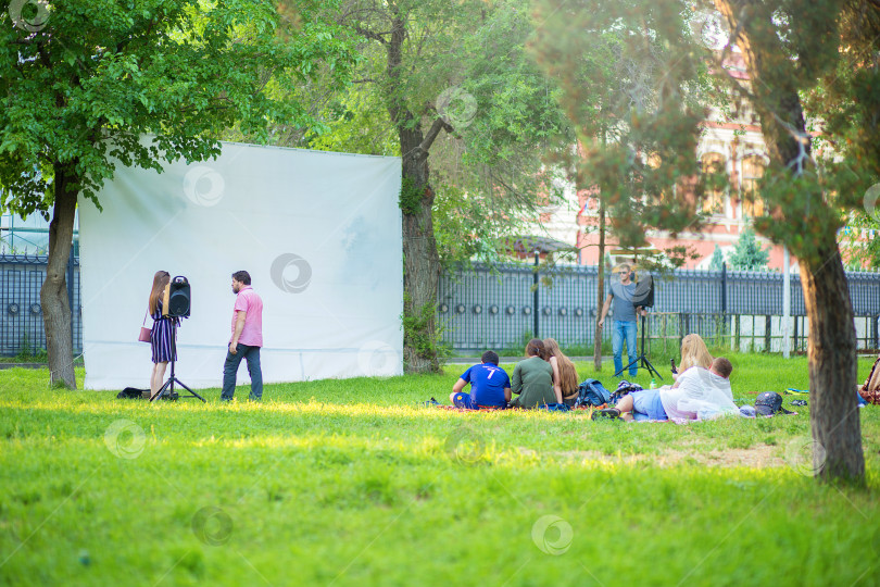 Скачать Волгоград, Россия, 30.05.2019: Сооружение кинотеатра под открытым небом в парке. Люди собираются на траве, чтобы посмотреть фильм фотосток Ozero