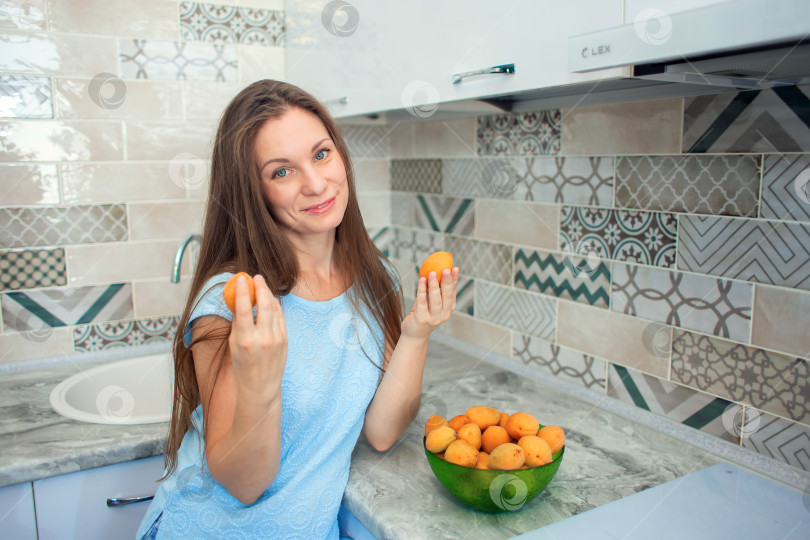 Скачать Девушка с длинными волосами на своей кухне собирает спелые абрикосы фотосток Ozero