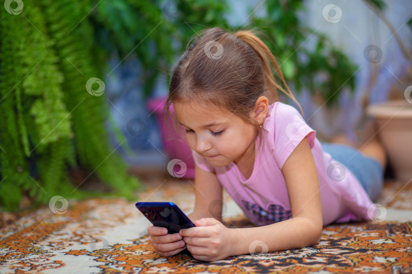 Скачать Девушка лежит на полу и играет на смартфоне. Ребенок и технология. Ребенок сидит дома и развлекается с телефоном. фотосток Ozero