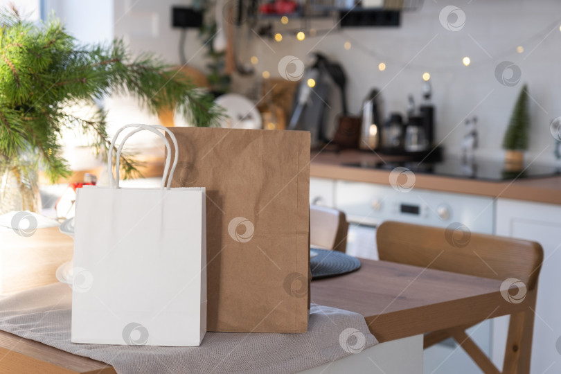 Скачать Макет бумажных упаковок лежит на кухонном сервированном столе, украшенном к Рождеству. Покупки и подарки, подарки и готовые блюда доставляются и готовятся к новому году фотосток Ozero