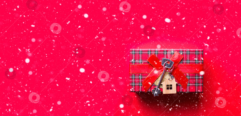 Скачать Ключ от дома с брелком коттедж. С Новым годом-красный фон со снегом, подарок, поздравительная открытка. Покупка, строительство, переезд, ипотека. пространство для копирования фотосток Ozero