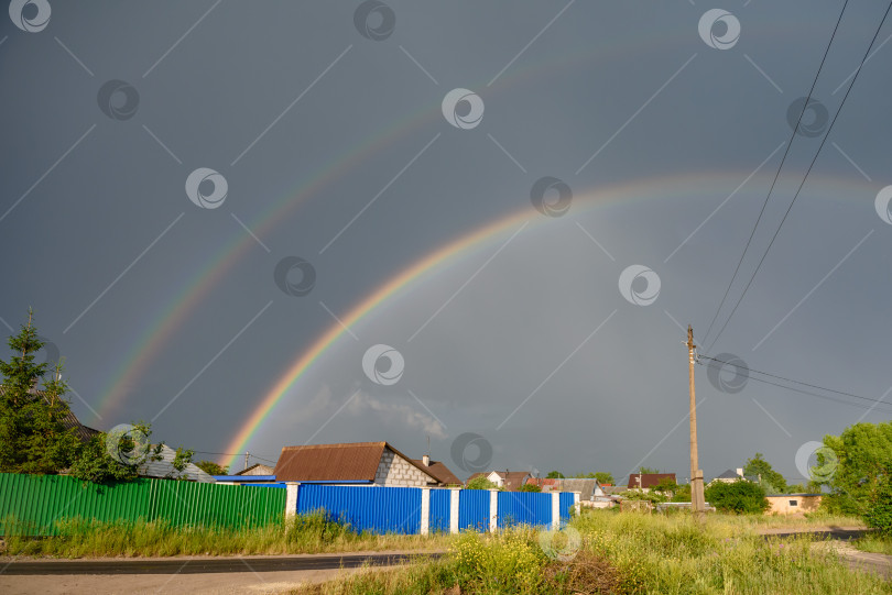 Скачать Двойная радуга на фоне дождливого неба над деревней фотосток Ozero