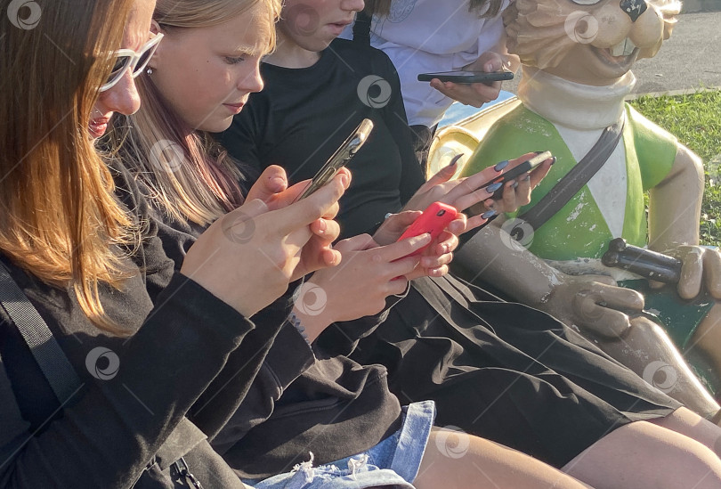Скачать Россия, Санкт-Петербург, август 2023 года: подростки, сидя на улице, проводят время за смартфонами. Концепция зависимости от телефонов и Интернета фотосток Ozero