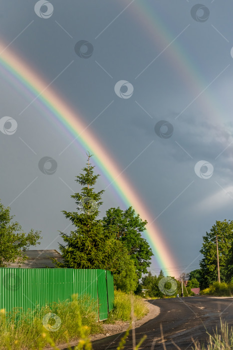 Скачать Двойная радуга на фоне дождливого неба над деревенской дорогой фотосток Ozero