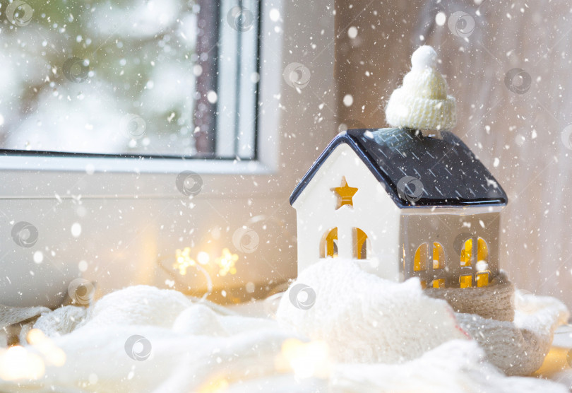 Скачать Уютный домик, закутанный в шапку и шарф в метель - декор подоконника. Зима, снег - утепление дома, защита от холода и непогоды, система отопления помещения. Праздничное настроение, Рождество, Новый год фотосток Ozero