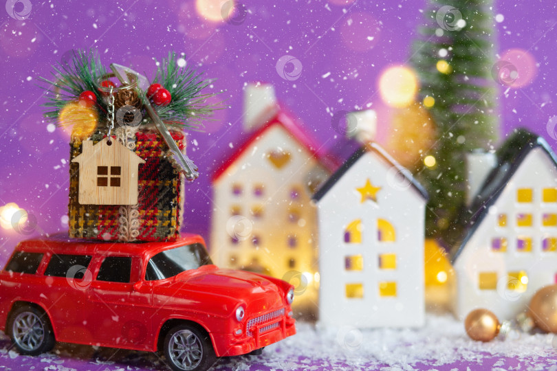 Скачать Красный ретро-автомобиль по снегу везет подарочную коробку с ключом от дома с брелоком для ключей, коттедж на крыше, мимо домов с гирляндами, рождественская елка. Фиолетовый фон. Уютный Новый год. Недвижимость, переезд, ипотека. фотосток Ozero