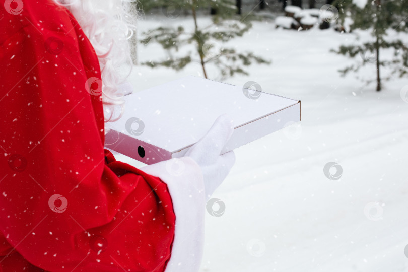 Скачать Белая коробка из-под пиццы в руках Деда Мороза в белых варежках, с бородой, в красном пальто. Рождественская доставка фаст-фуда. Акция в канун Нового года. Работаем в праздничные дни в сфере общественного питания. Место для копирования, макет фотосток Ozero
