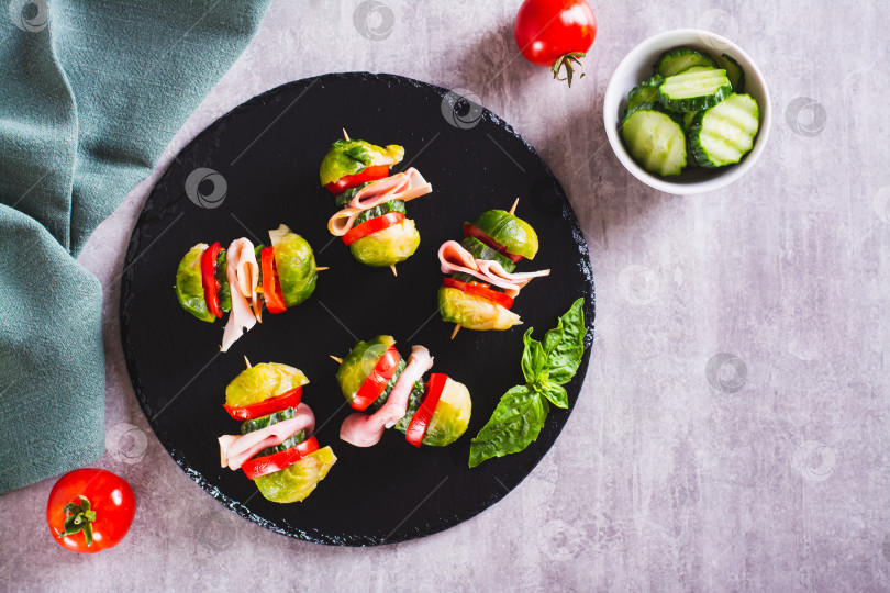 Скачать Слайдеры с брюссельской капустой, помидорами, огурцами и беконом на грифельной доске вид сверху фотосток Ozero