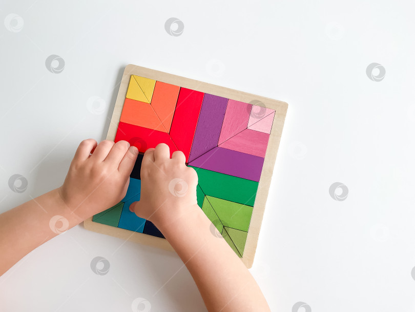 Скачать детская рука собирает разноцветную деревянную мозаику на белом фоне. фотосток Ozero