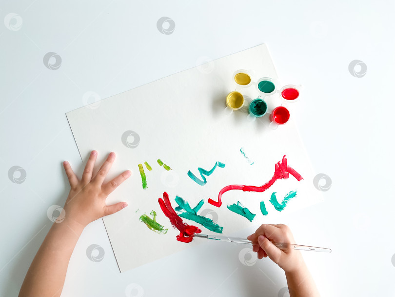 Скачать маленький ребенок рисует красками и кистью на белом столе. фотосток Ozero