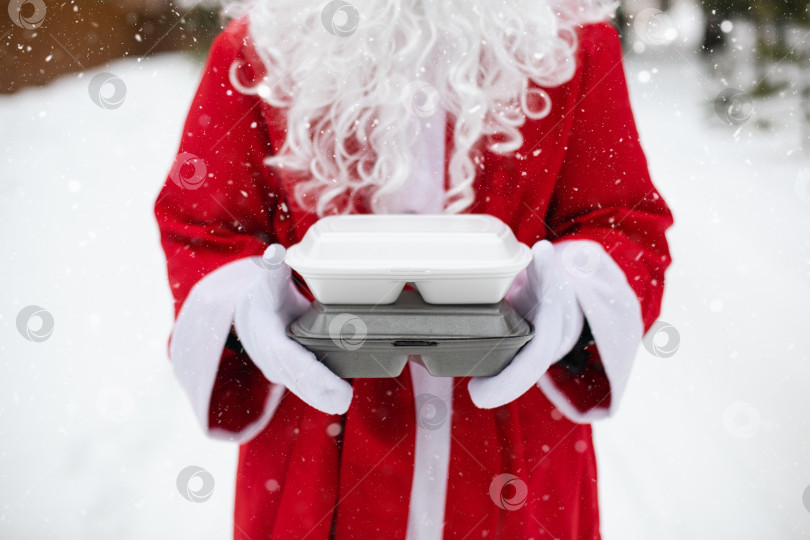 Скачать Контейнеры службы доставки еды в руках Санта-Клауса на открытом воздухе в снегу. Акция в канун Рождества. Готовый горячий заказ, одноразовая пластиковая коробка. Организация питания на новогодние праздники. Пространство для копирования, макет фотосток Ozero