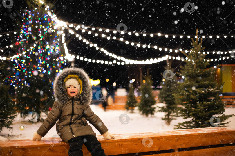 Скачать Маленькая девочка вечером катается на коньках по катку, украшенному гирляндами, рождественскими елками и пихтой. Праздничное настроение, Рождество, Новый год, каникулы, активные зимние виды спорта и образ жизни фотосток Ozero
