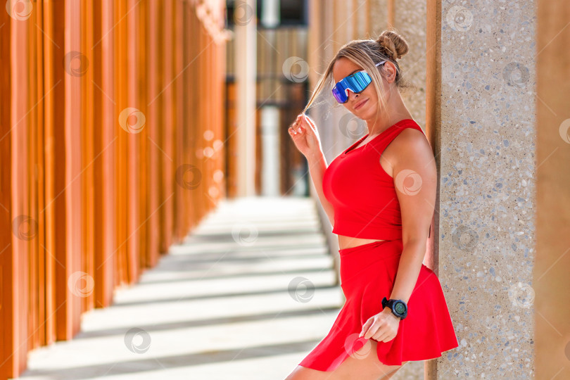 Скачать Женщина со светлыми волосами в красной спортивной одежде позирует на открытом воздухе на стадионе. Спорт. Здоровый образ жизни. фотосток Ozero
