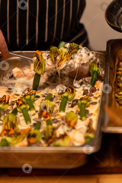 Скачать Повар выкладывает лосось с грибами в сливочном соусе под цветки цуккини на тарелку фотосток Ozero