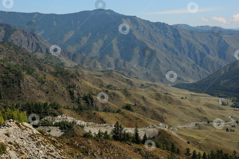 Скачать Вид с вершины перевала на асфальтированную дорогу, спускающуюся в живописную долину солнечным летним днем. фотосток Ozero