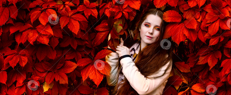 Скачать женщина с длинными рыжими волосами и ярким макияжем возле красных листьев живой изгороди фотосток Ozero