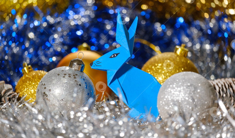 Скачать бумажный голубой кролик оригами и рождественские шары на фоне блестящей мишуры и боке фотосток Ozero