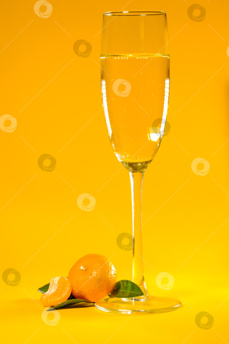 Скачать маленький спелый мандарин с зелеными листьями и бокалом шампанского на желтом фоне фотосток Ozero