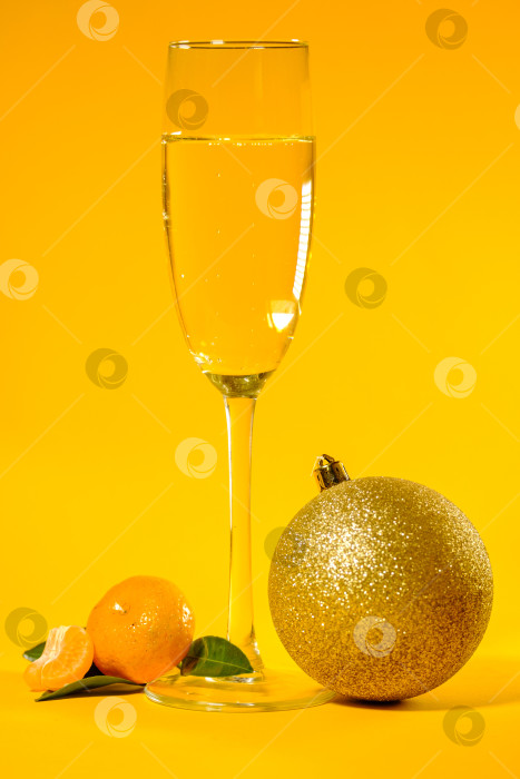 Скачать маленький спелый мандарин с зелеными листьями, рождественским шаром и бокалом шампанского на желтом фоне фотосток Ozero