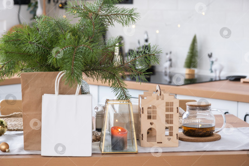 Скачать Макет бумажных упаковок лежит на кухонном сервированном столе, украшенном к Рождеству. Покупки и подарки, презенты и готовые блюда доставляются и готовятся к новому году фотосток Ozero