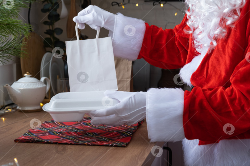 Скачать Сервис доставки еды на дом в контейнерах в руках Санта-Клауса ставит ее на кухонный стол и уносит. Готовый горячий заказ, кейтеринг на Рождество, новогодние праздники. фотосток Ozero