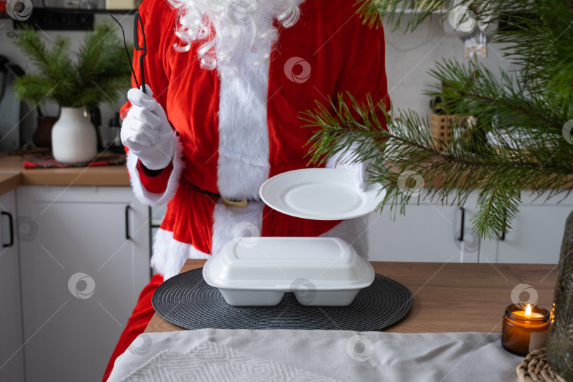 Скачать Сервис доставки еды на дом в контейнерах в руках Деда Мороза ставит их на кухонный стол и уносит. Готовый горячий заказ, кейтеринг на Рождественские, новогодние праздники. фотосток Ozero